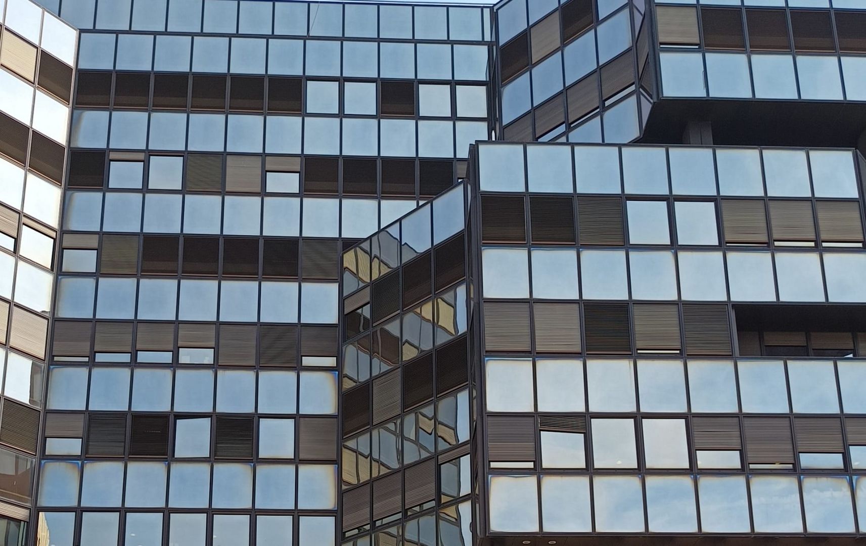 Glass facade of a big building with lines of blinds down.